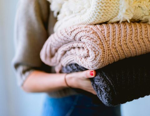 Person holding neatly folded knitted sweaters, representing fresh laundry delivery service.