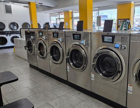 Row of modern stainless steel commercial washing machines inside a bright laundromat.