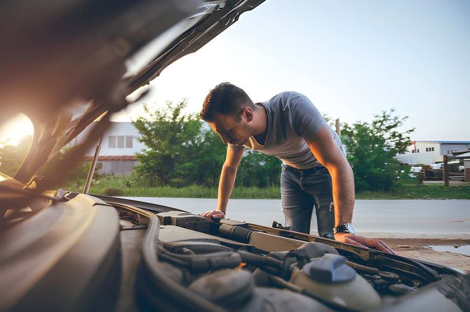 Man looking under the hood of a broken down car