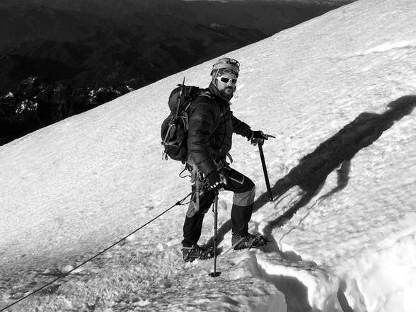Mountaineer in black and white, ascending a snowy slope using an ice axe.