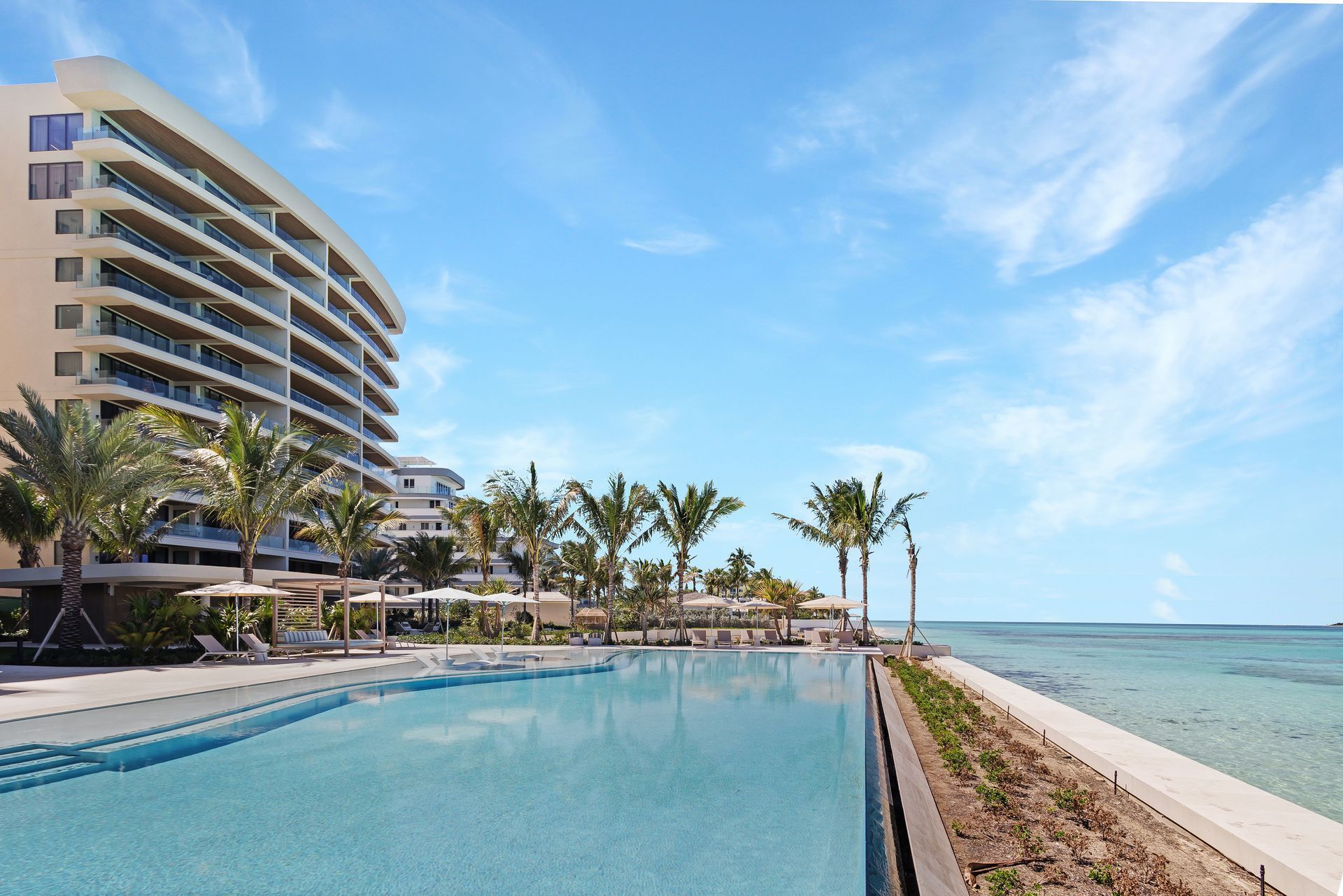 Aqualina in Nassau. Luxury resort with pool and ocean view, palm trees, blue sky.
