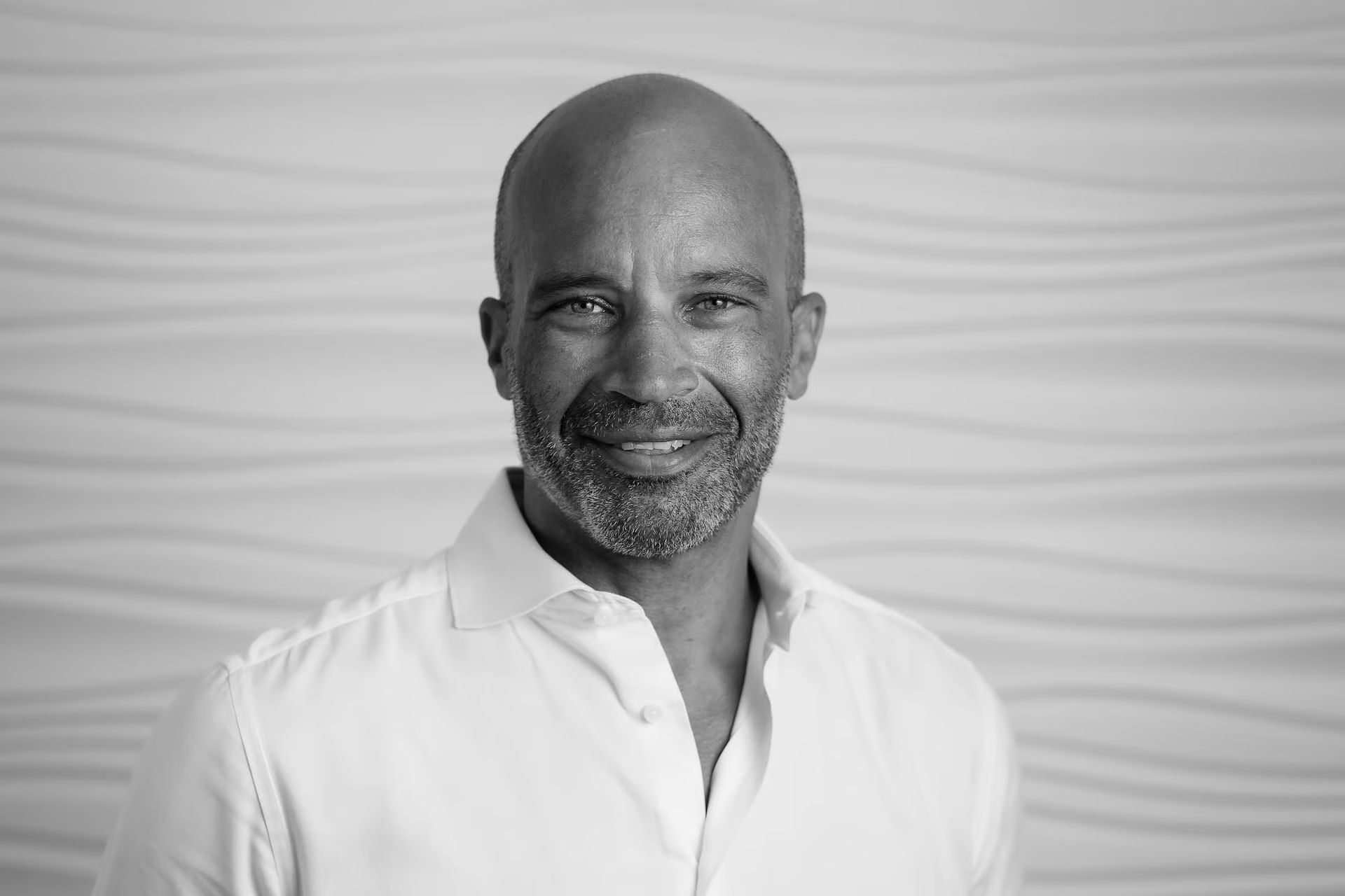 Jason Kinsale  smiling in a white shirt, against a textured white background.