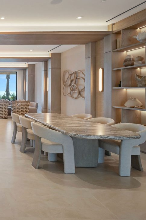 Aqualina in Nassau. Dining area with large stone table, beige chairs, built-in shelves, and artwork.