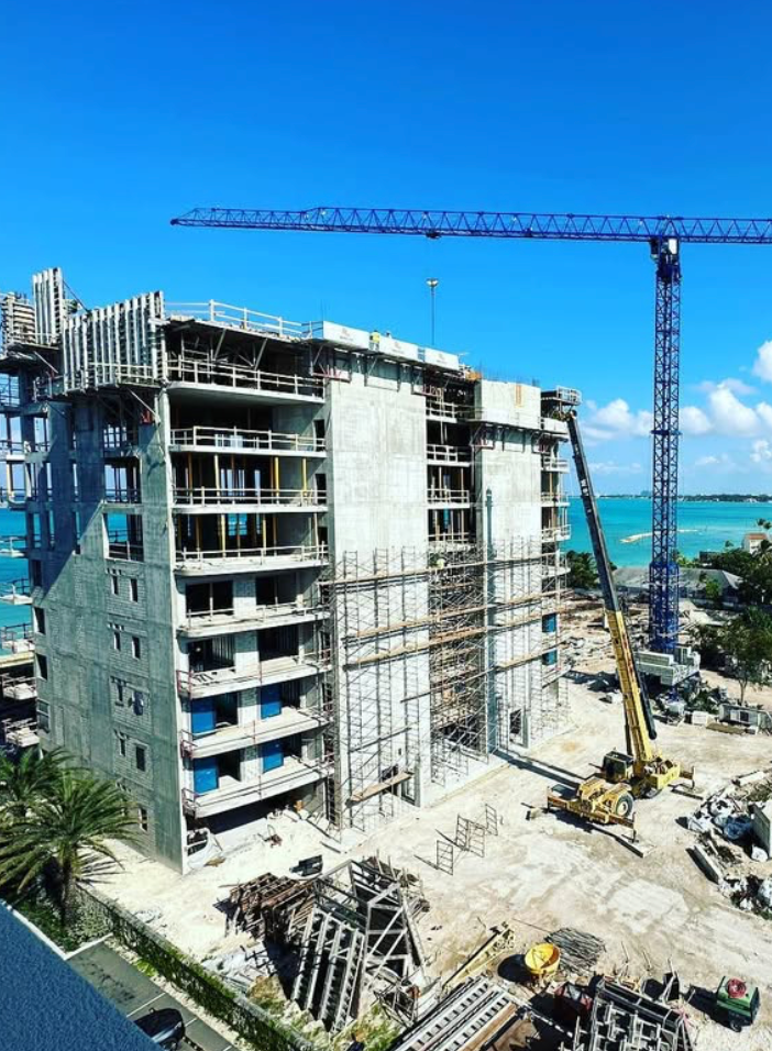 Construction of a multi-story building with a blue crane and ocean backdrop.