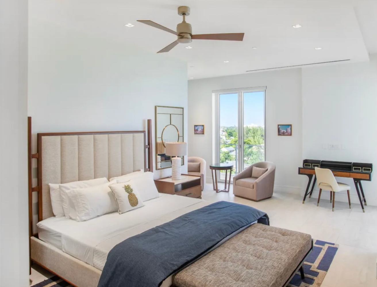 Spacious white bedroom with a bed, desk, chairs, and a view of the outdoors.