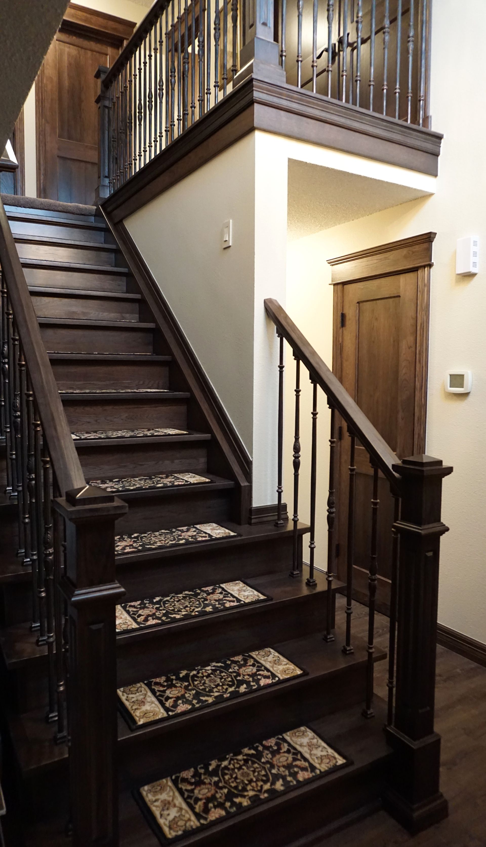 Wooden staircase with patterned carpet runners, leading to a landing with a wooden door.
