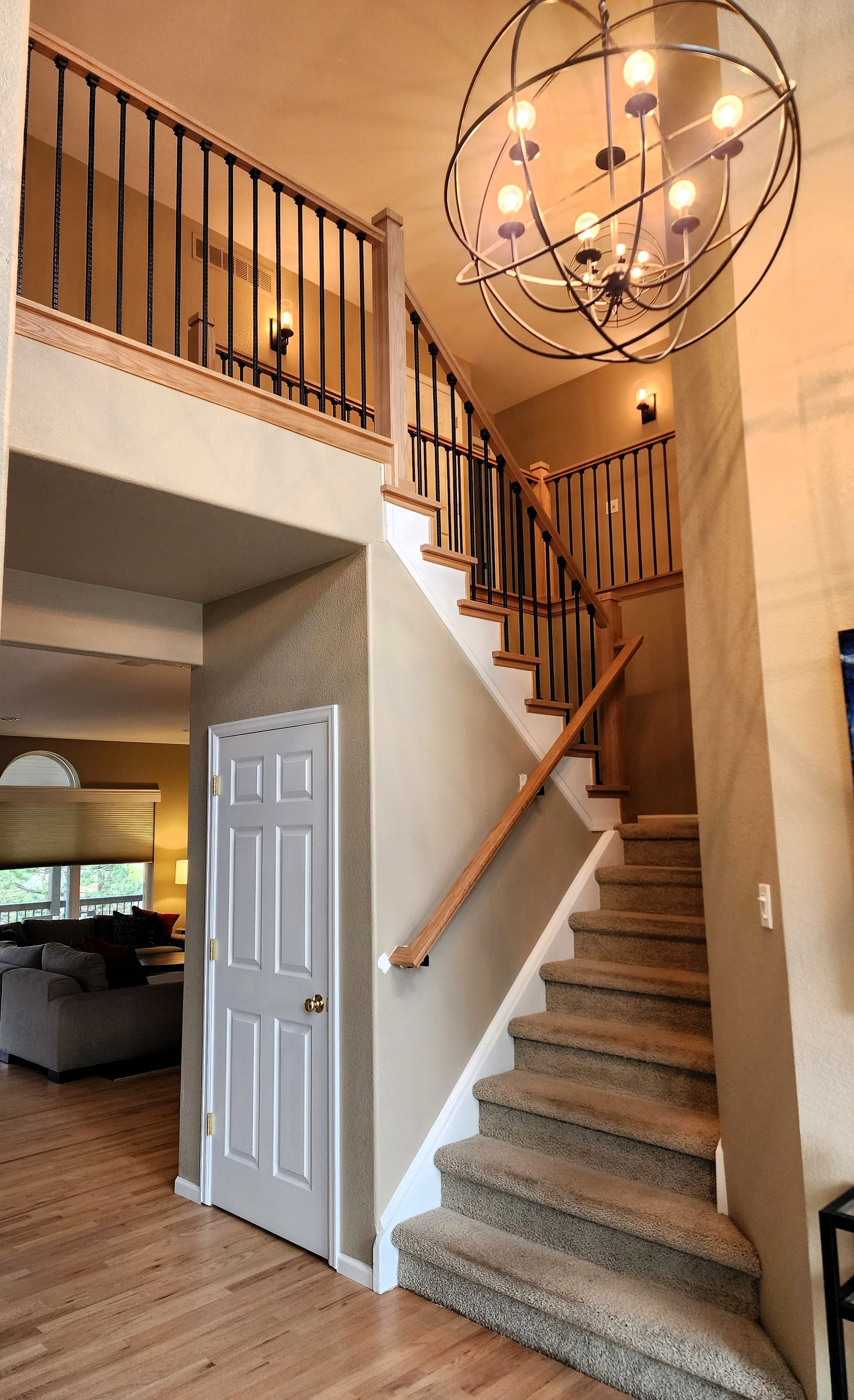 Staircase with carpeted steps leading to a second-floor landing. Black iron railing and a large orb light fixture.