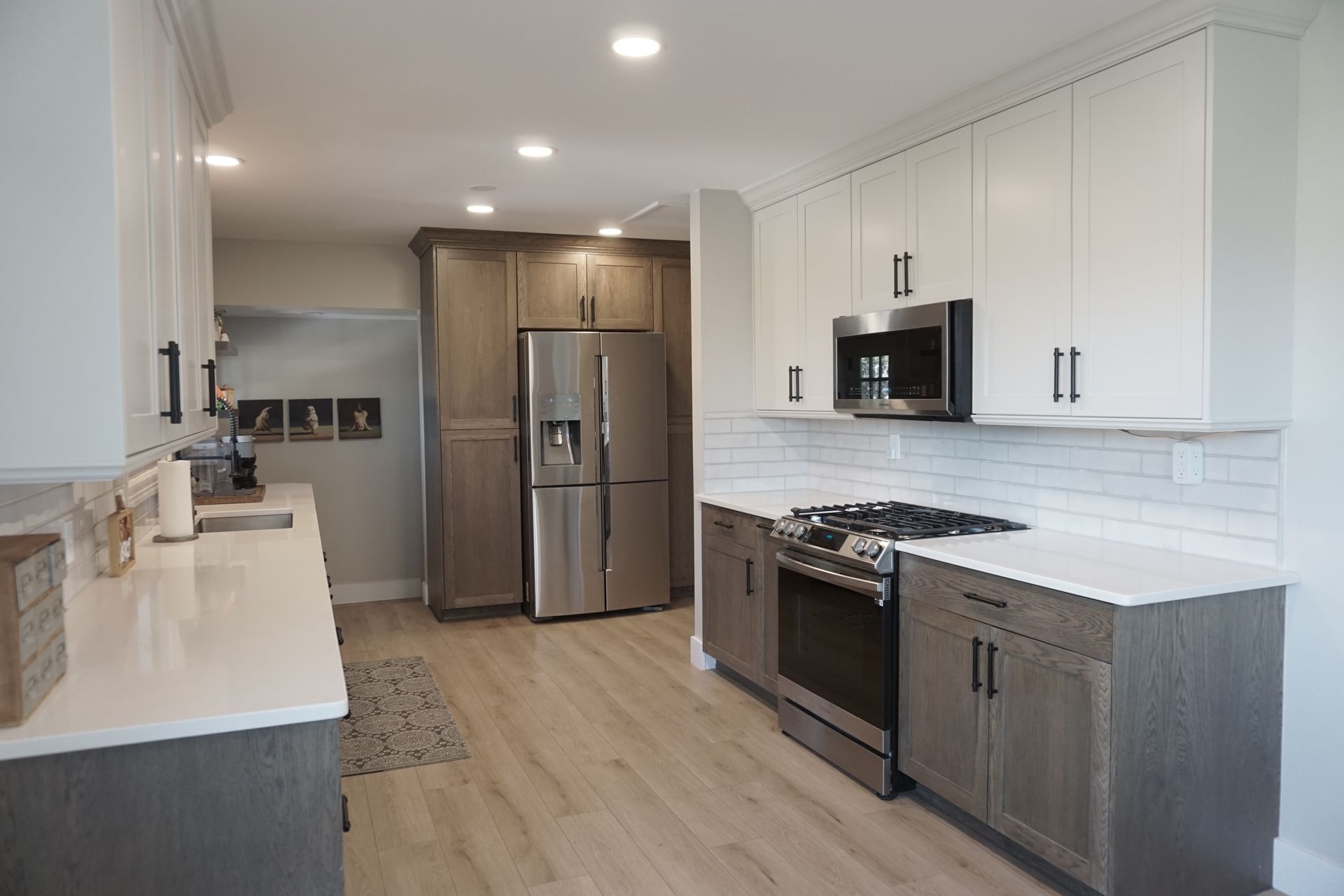 Modern kitchen with white and gray cabinets, stainless steel appliances, and light wood flooring.