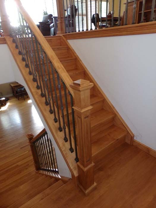 Wooden staircase with ornate black iron spindles. Sunlight streams through windows.
