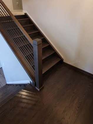 Wooden staircase with dark brown treads and railing against white walls.