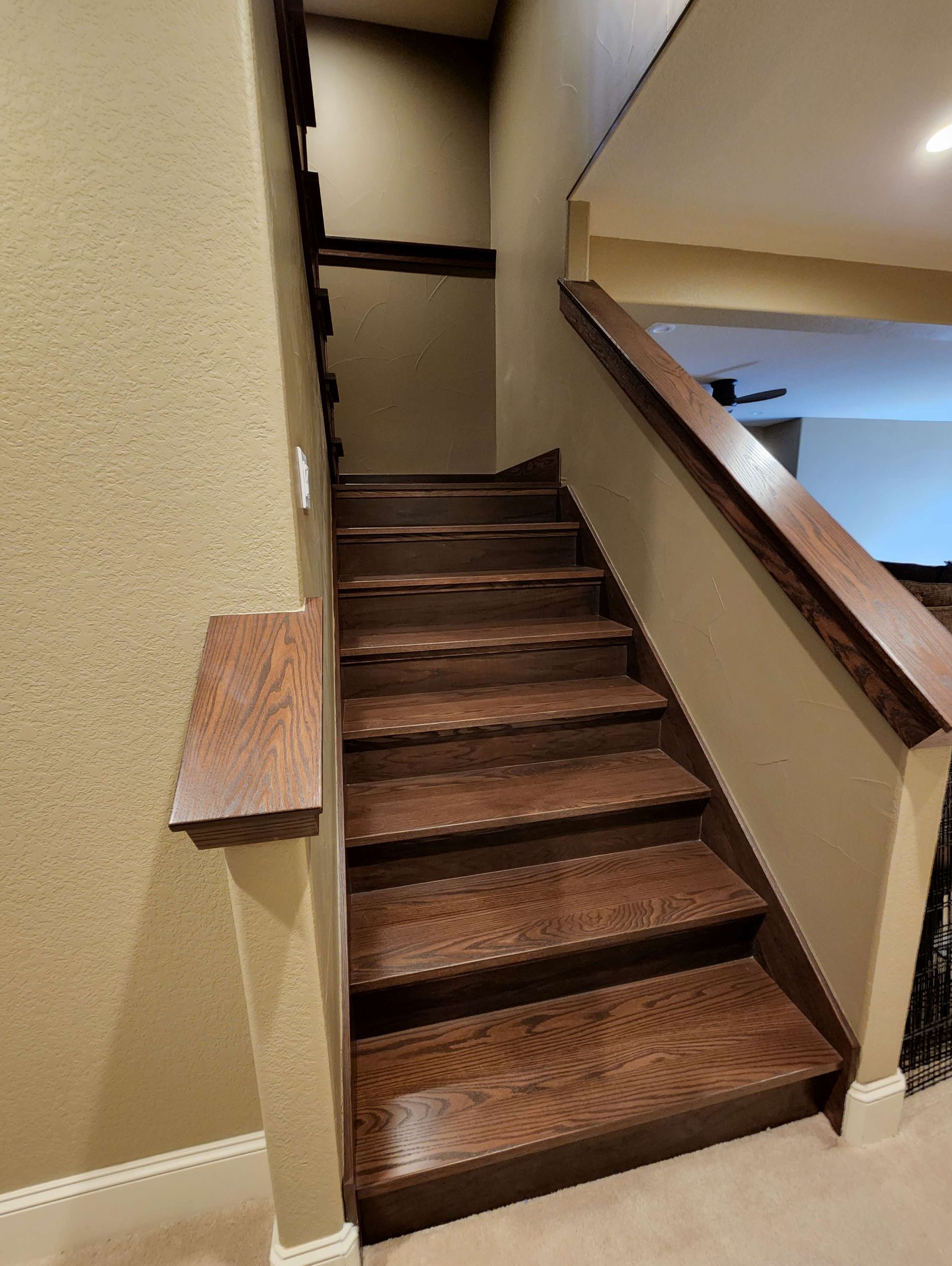 Wooden staircase with brown treads and handrails against beige walls.