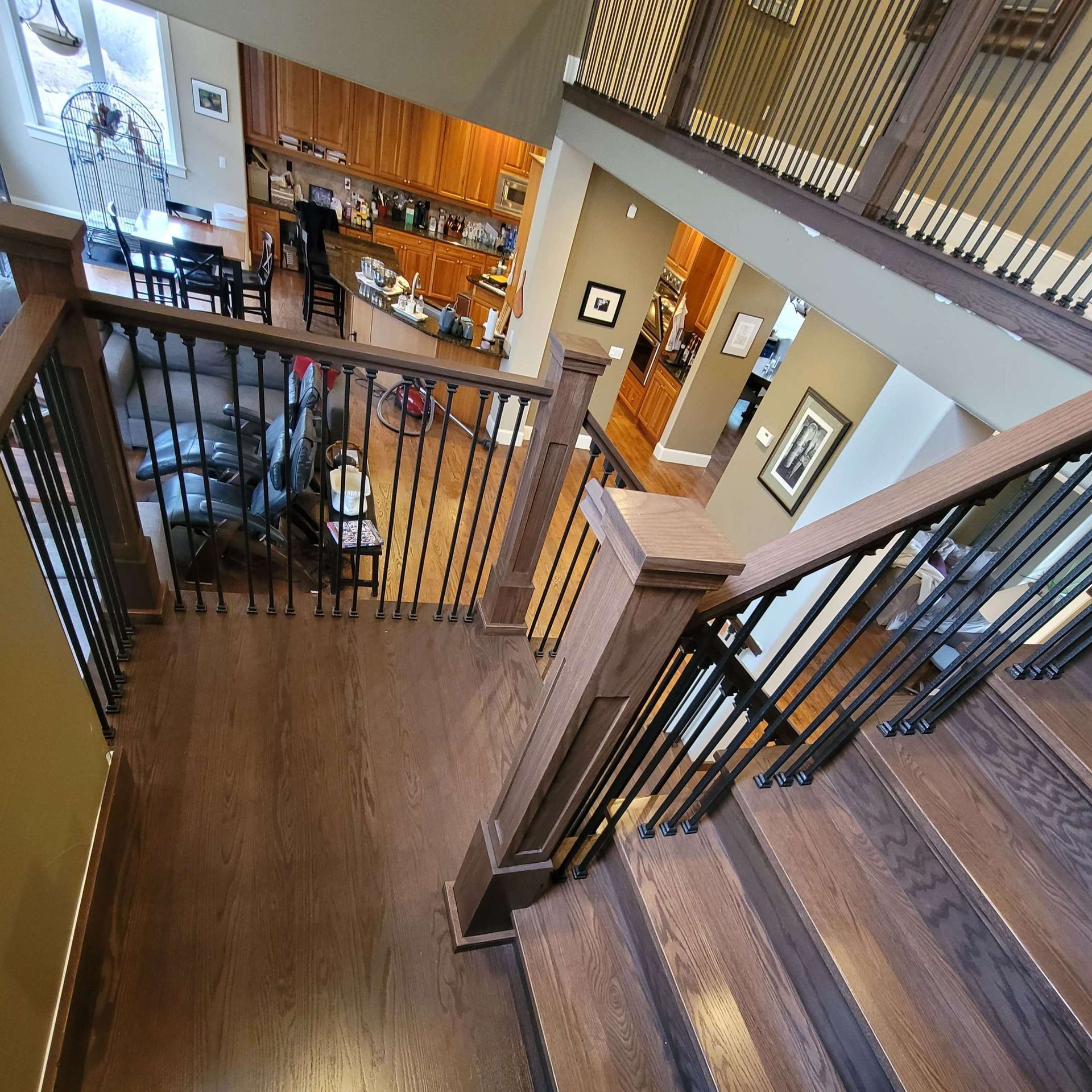 View from a staircase landing. Dark wood stairs and railing with black spindles overlook a living room.