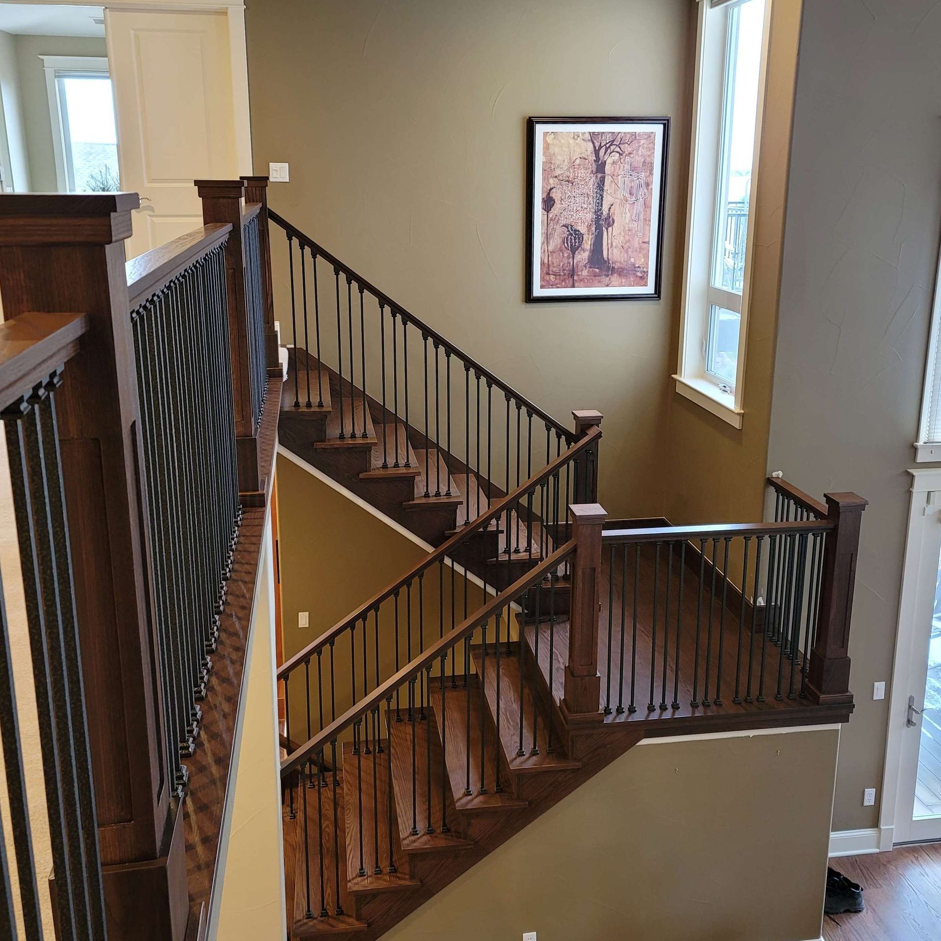 Staircase with wooden steps and railing, black iron balusters, tan walls, and a framed picture.