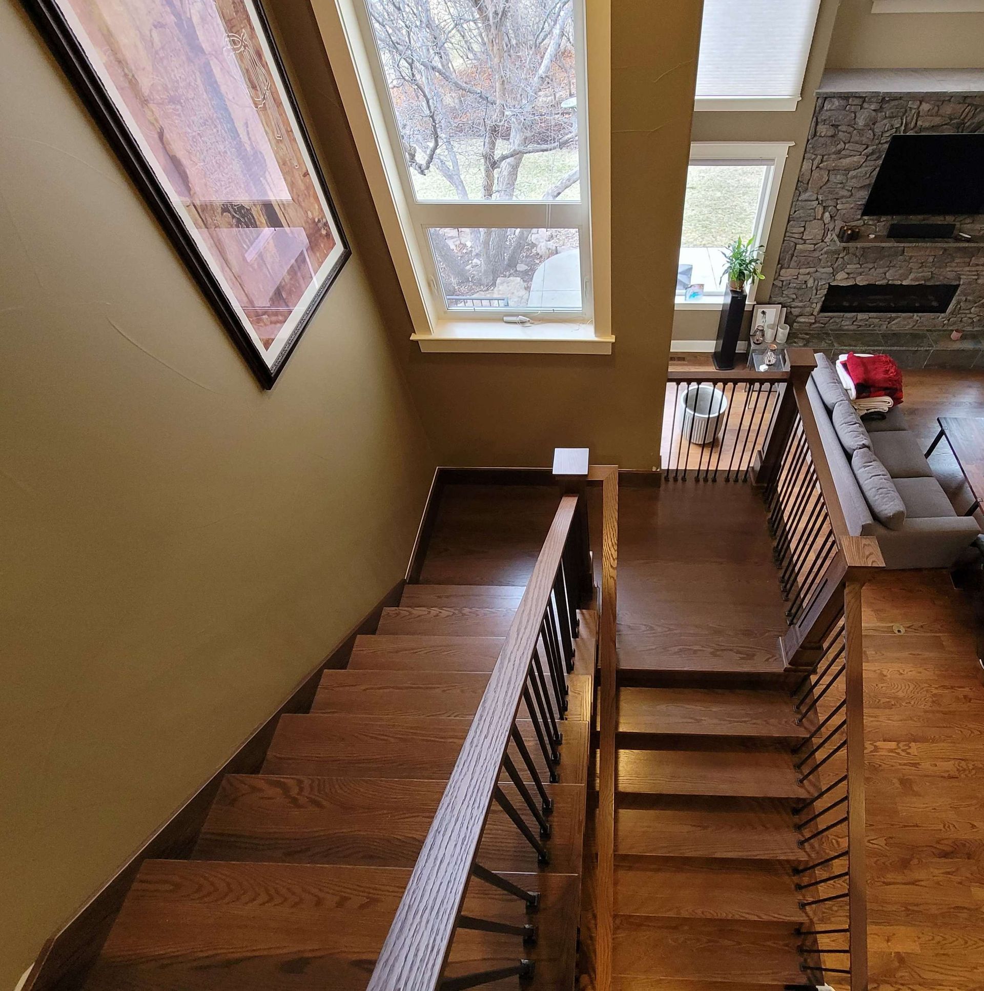 Wooden staircase descending, leading to a living area with a sofa, fireplace, and window.