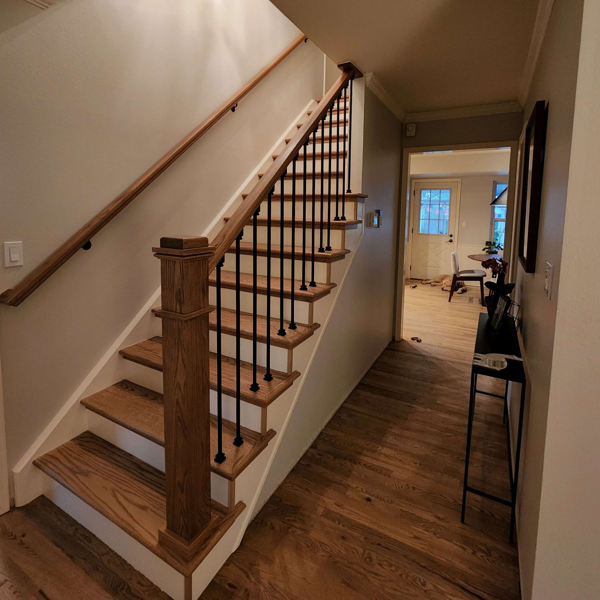 Wooden staircase with black metal balusters, wooden handrails, and a hallway with a wooden floor.