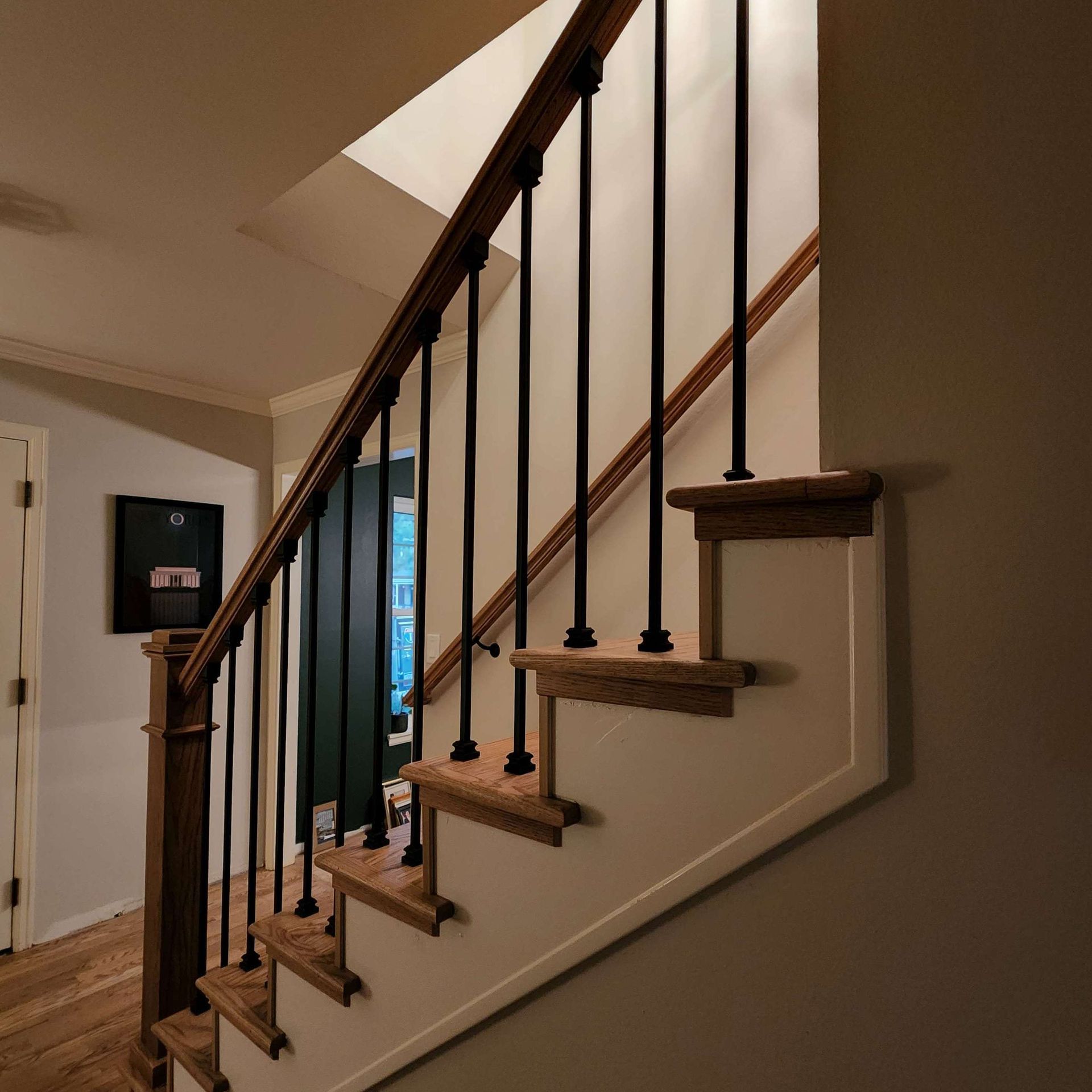 Staircase with wooden steps and railing, black spindles, and white wall. Door visible at top.
