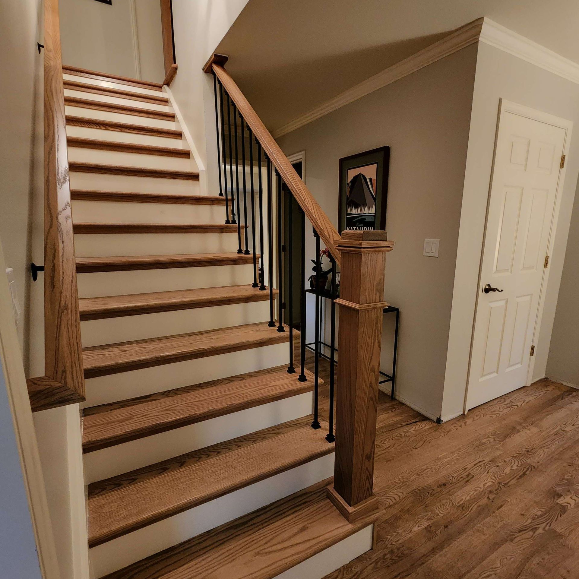 Wooden staircase with white risers, black spindles, and wood handrails, leading to an upper level.