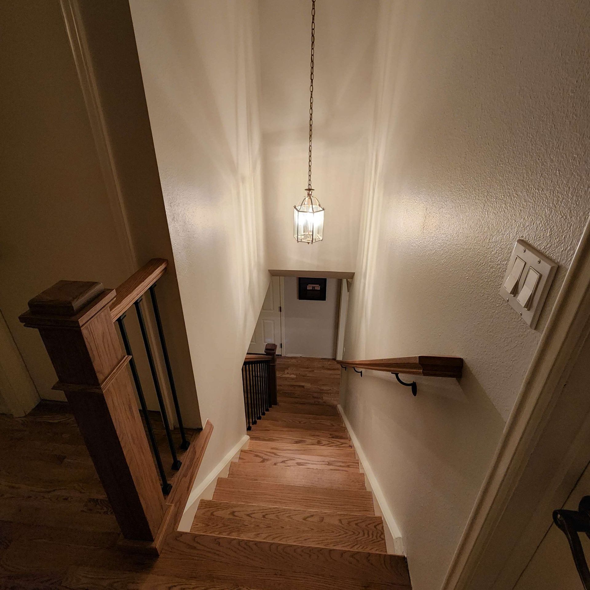 Staircase with wooden steps and railing leading downwards. Pendant light hangs from ceiling.