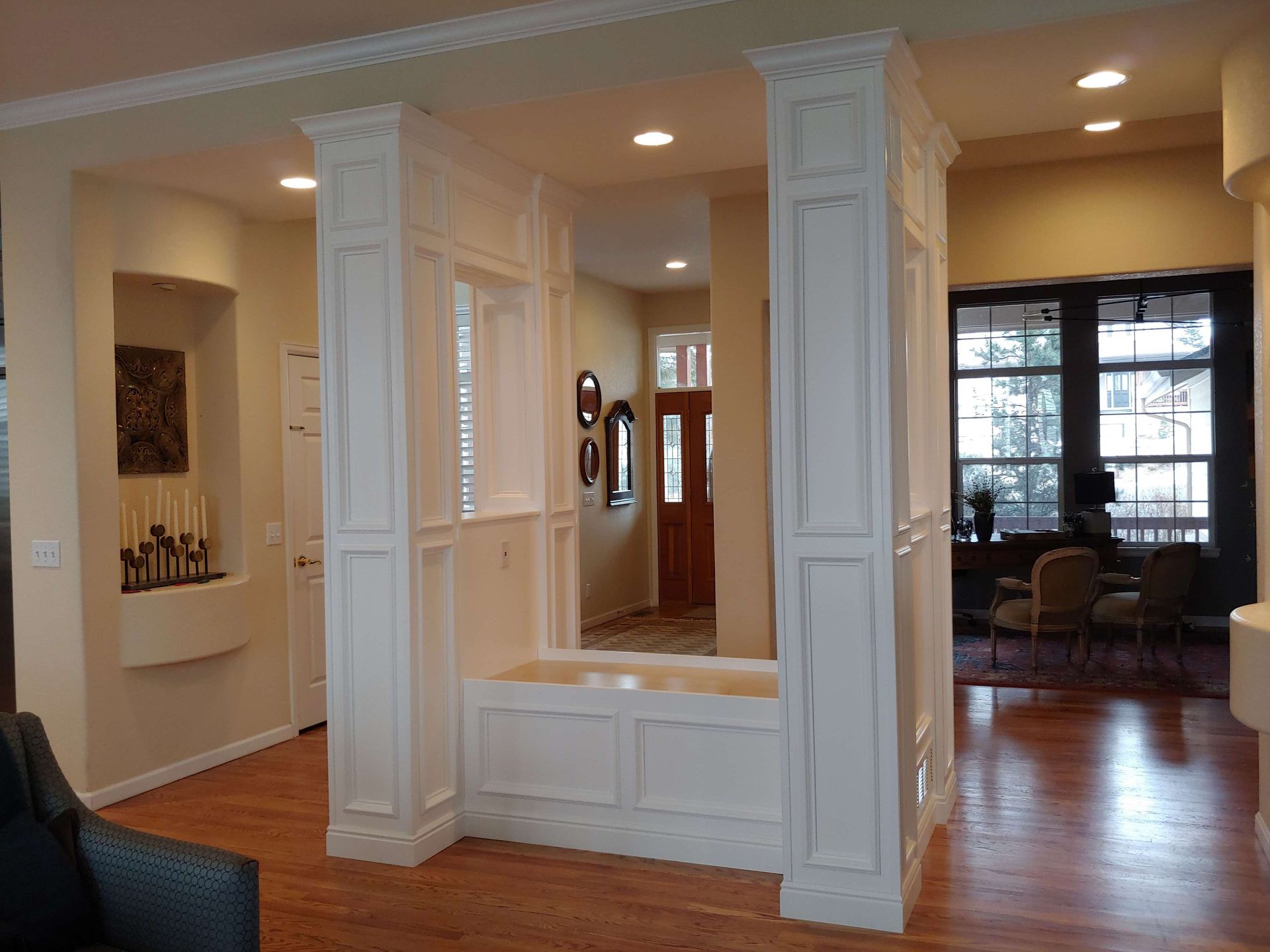 Interior room with white pillars, built-in bench, and doorway leading to an entryway with a wood door.