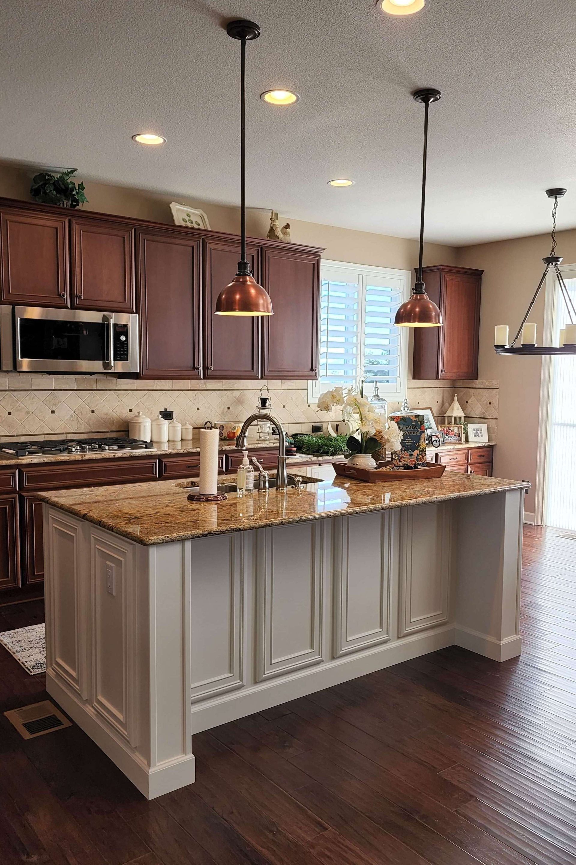Kitchen with a white island, granite countertop, copper pendant lights, and dark wood cabinets.
