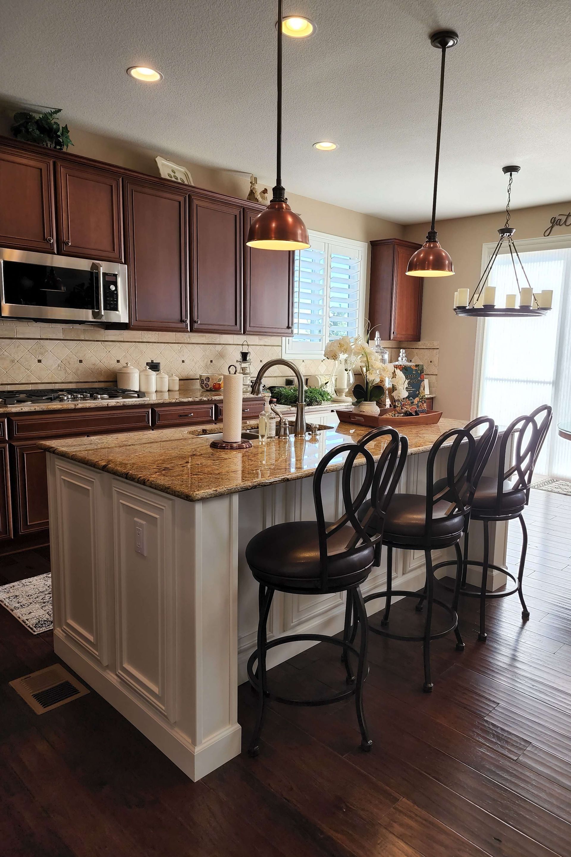 Kitchen with dark wood cabinets, a white island, and copper pendant lights.