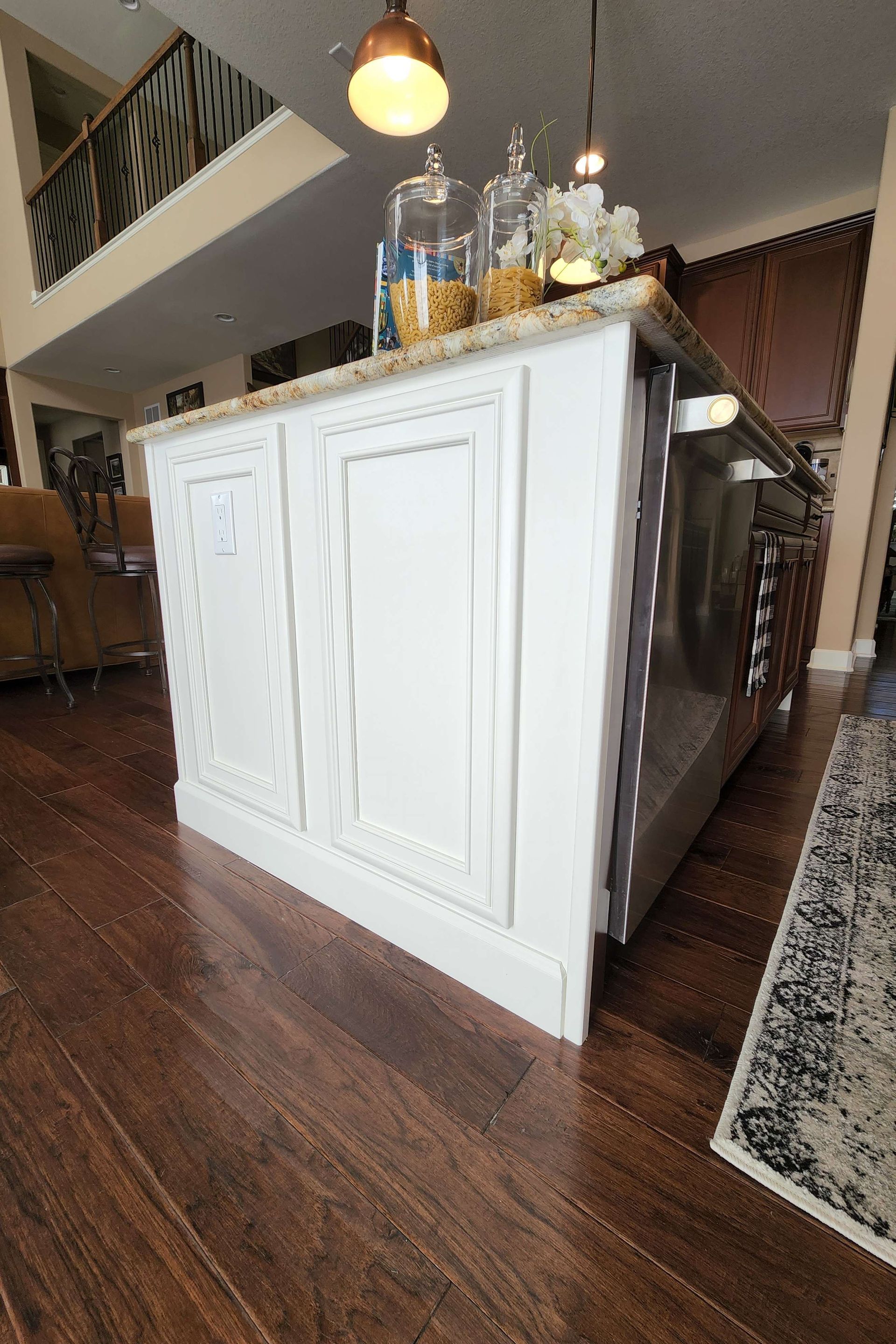 White kitchen island with granite countertop, dark wood floor, and jars.
