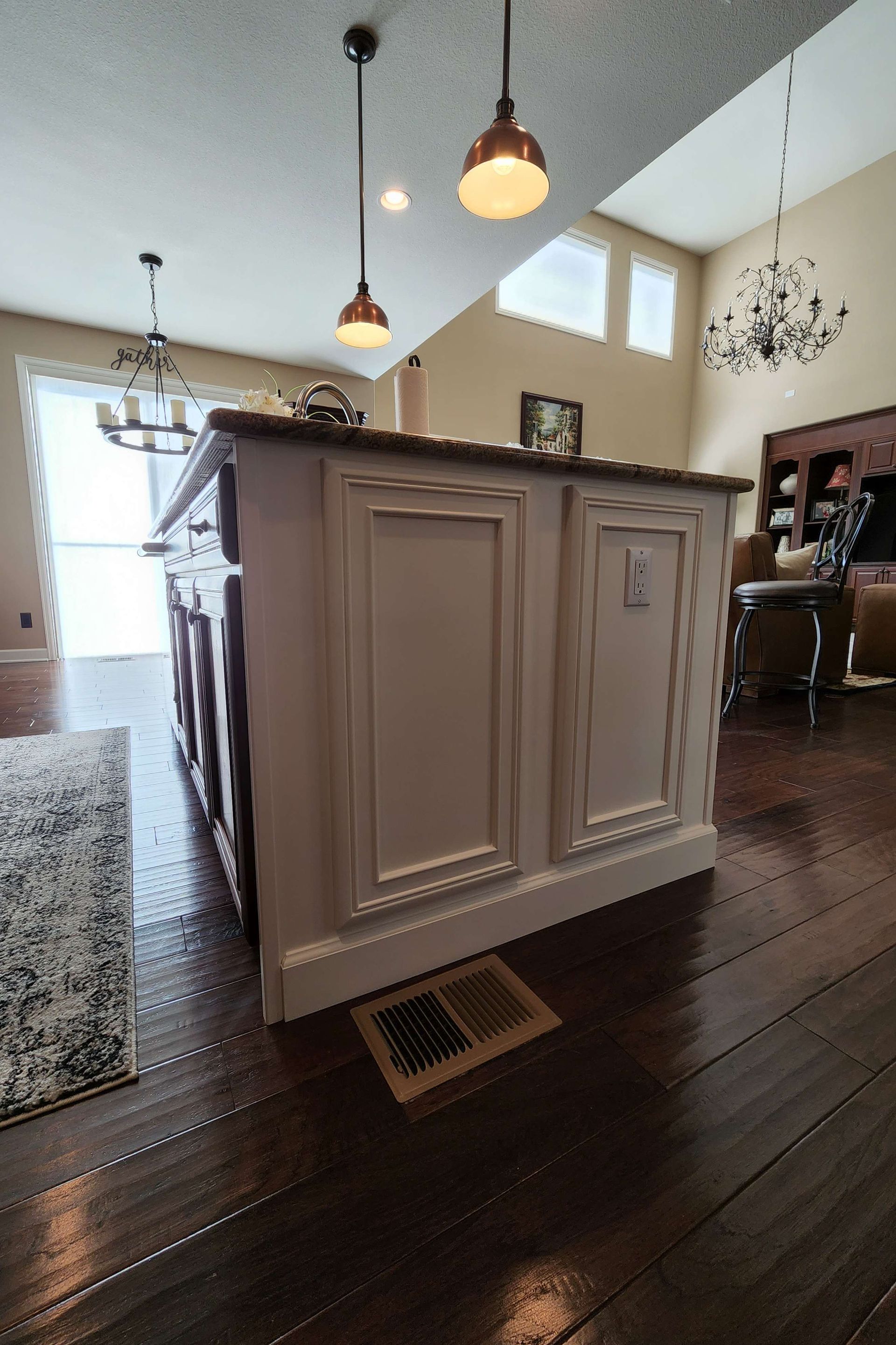 Kitchen island with white paneling and dark countertop. Copper pendant lights hang above.
