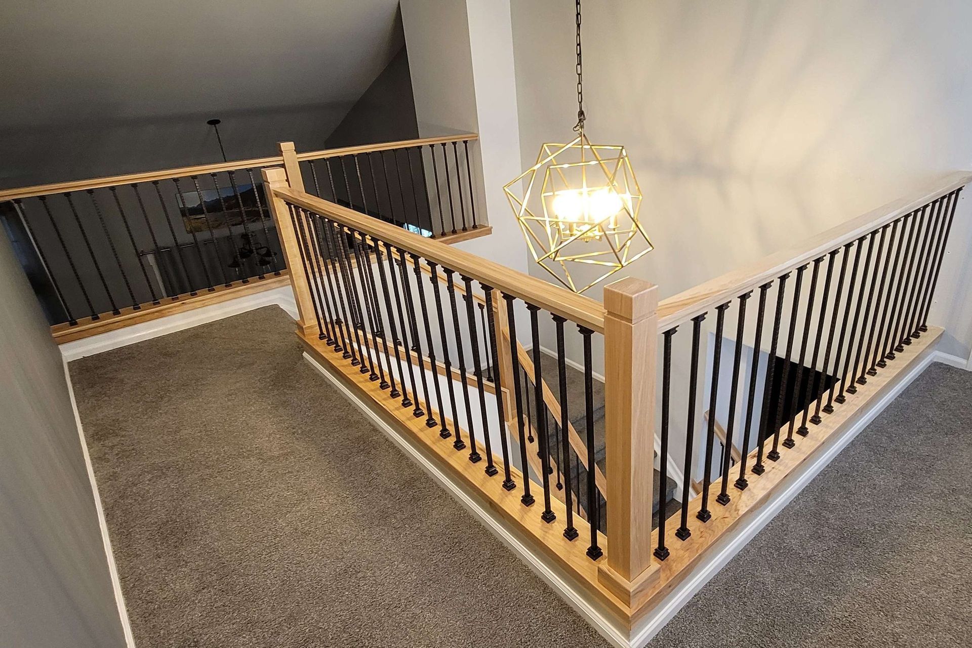 Staircase with light-colored wood railings and black vertical spindles. A modern geometric light fixture hangs above.