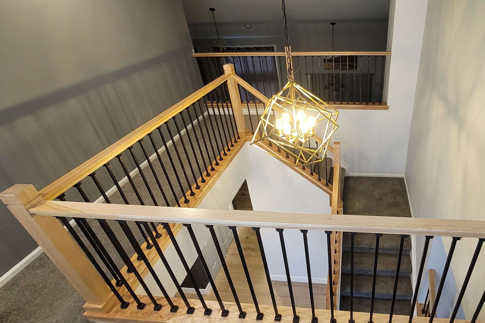 Staircase with light wood railing, black spindles, and a geometric chandelier.