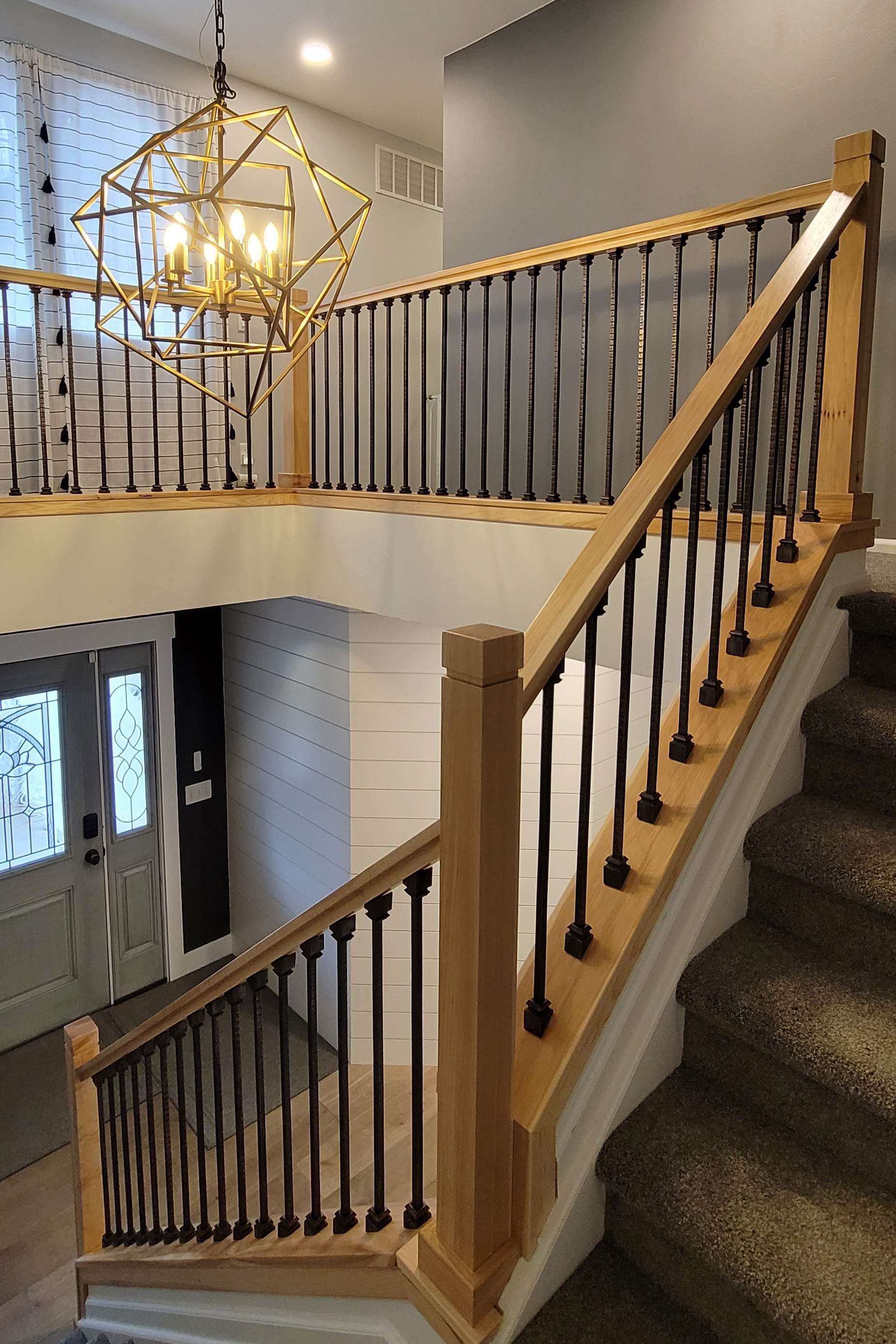 Staircase with wooden handrails, black spindles, and a geometric chandelier.
