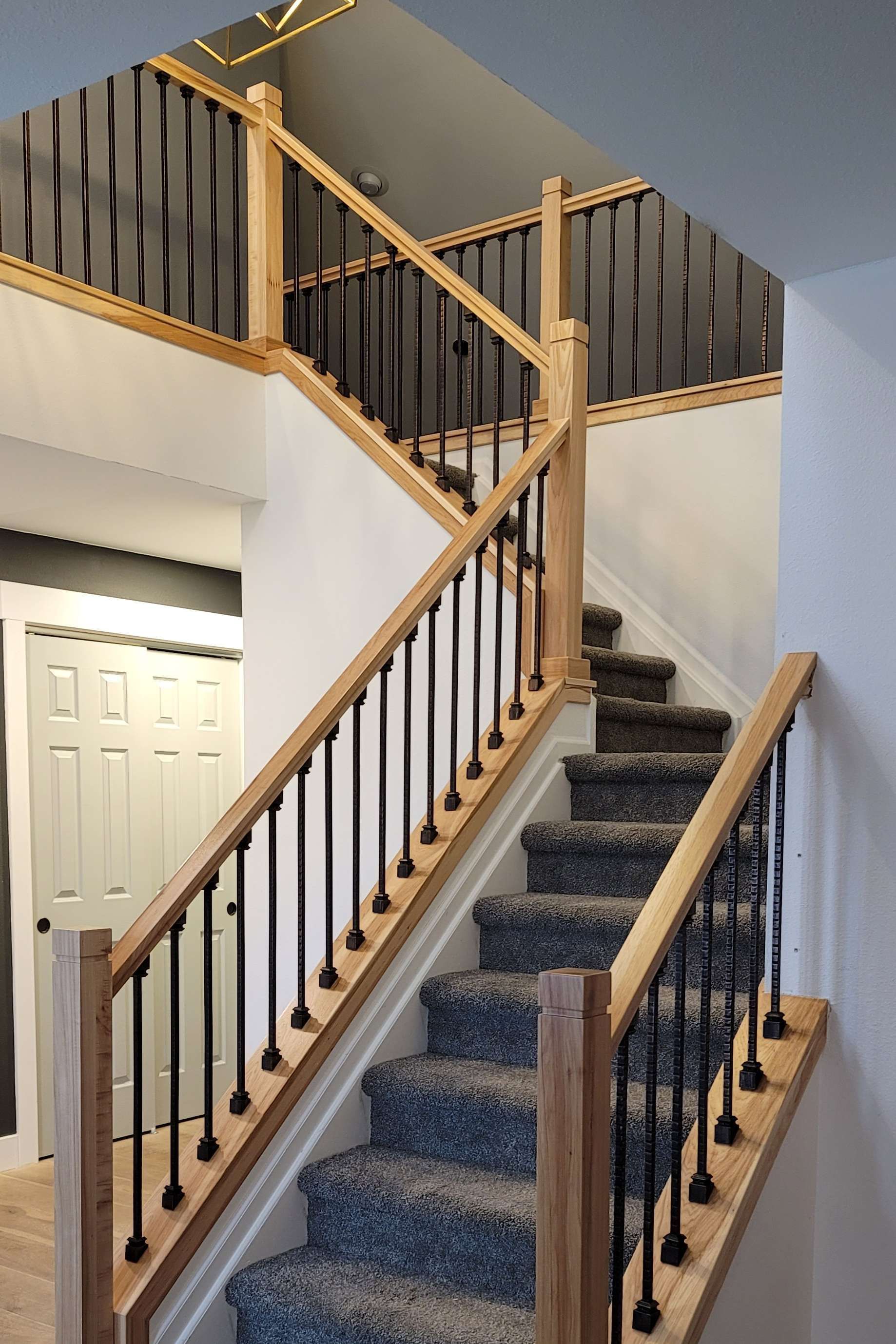 Staircase with light wood and black spindles. Carpeted stairs. Handrails along both sides.