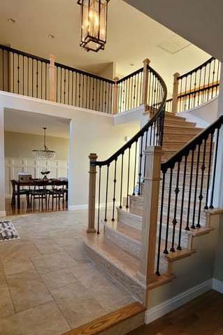 Two-story foyer with wooden staircase, black metal railings, and a chandelier, leading to a dining room.