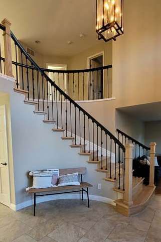 A two-story entryway with a curved staircase, black railing, light wood accents, and a bench.