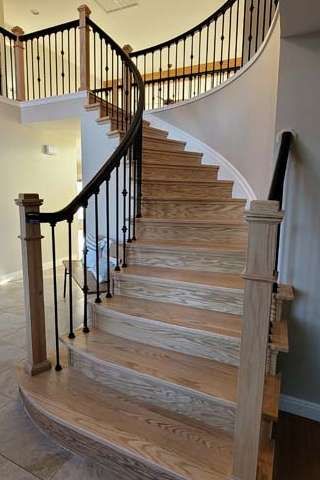 Wooden curved staircase with black railing and light-colored walls.