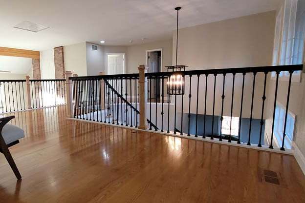 A light-filled interior with hardwood floors, a black railing, and a pendant light.