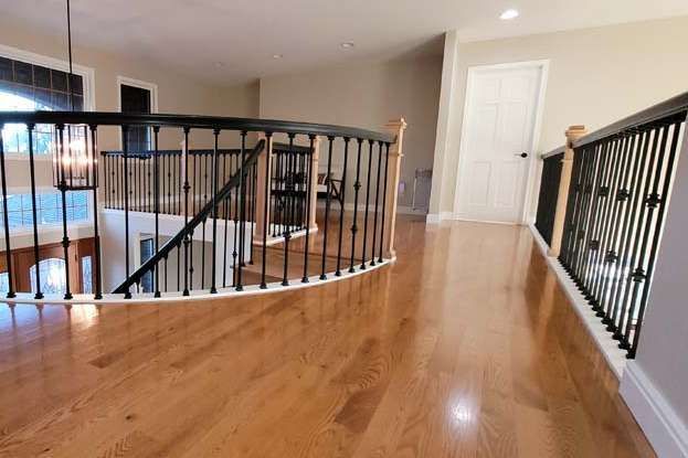 Wooden hallway with black railing overlooking a staircase. A white door is at the end.