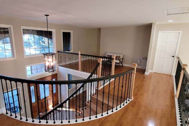 Interior view of a two-story home with a curved black railing, hardwood floors, and a hanging light fixture.