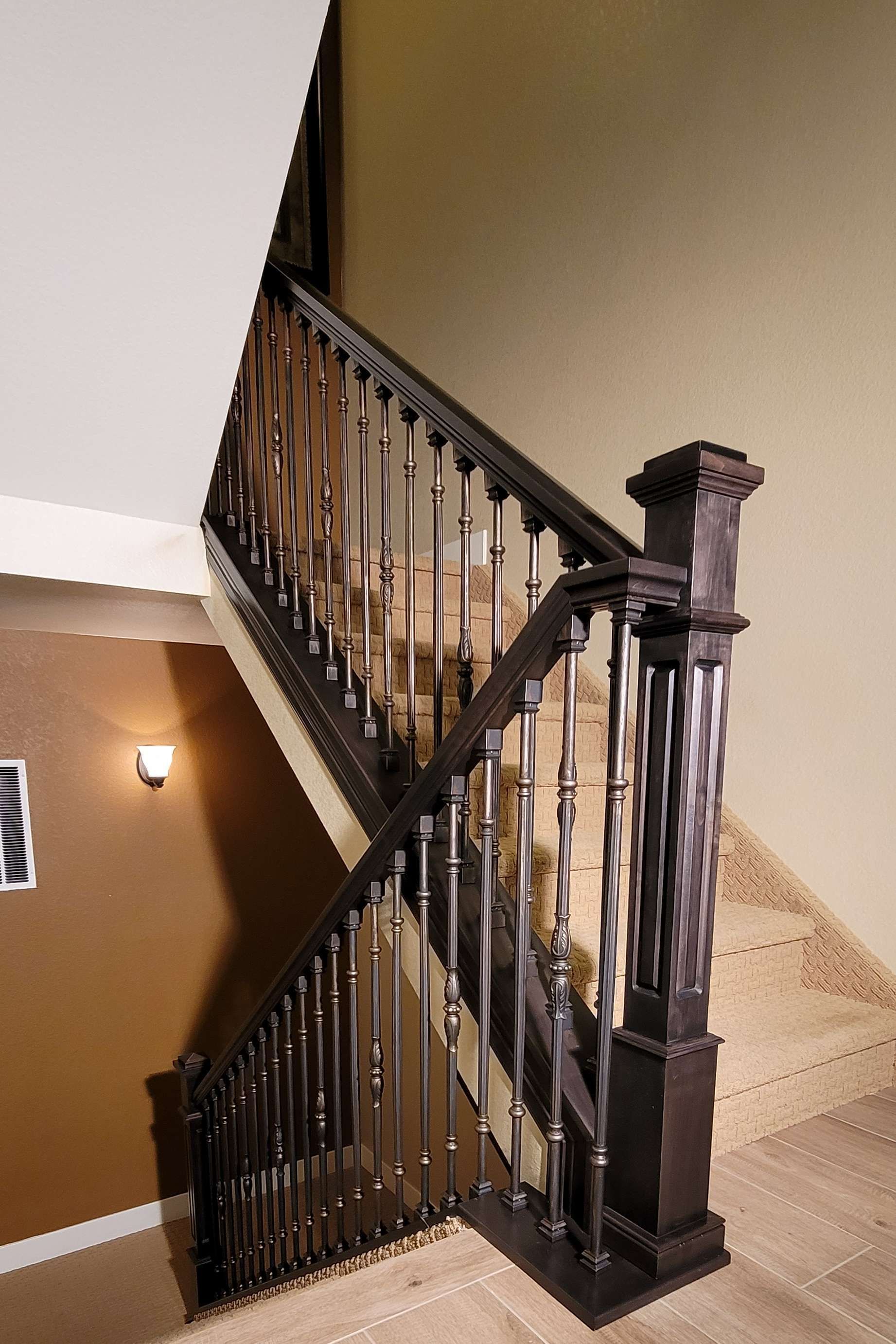 Staircase with dark wooden banister and spindles, tan carpet, and beige walls.