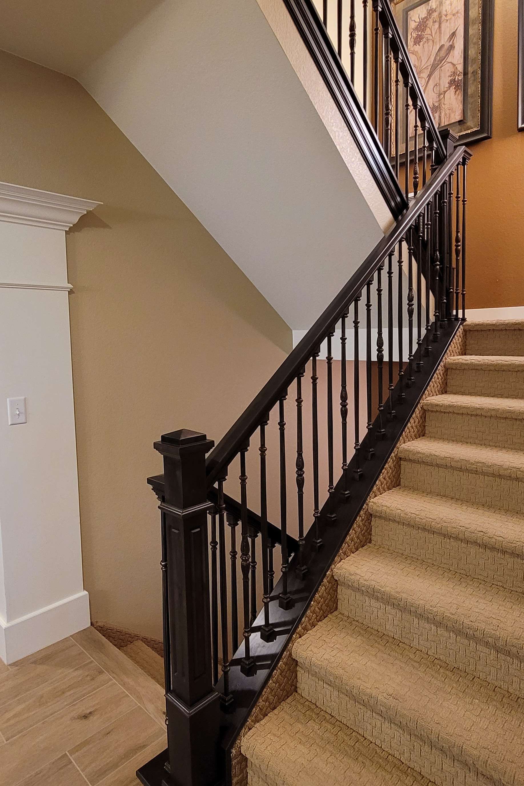 Staircase with black railing and tan carpeted steps. White and tan walls.