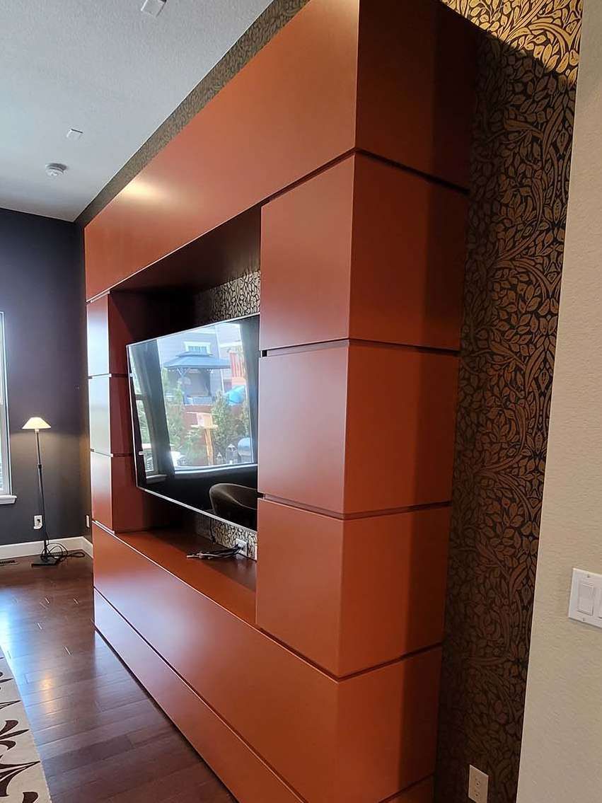 Built-in orange media cabinet with TV; brown patterned wall on right, dark wood floor.
