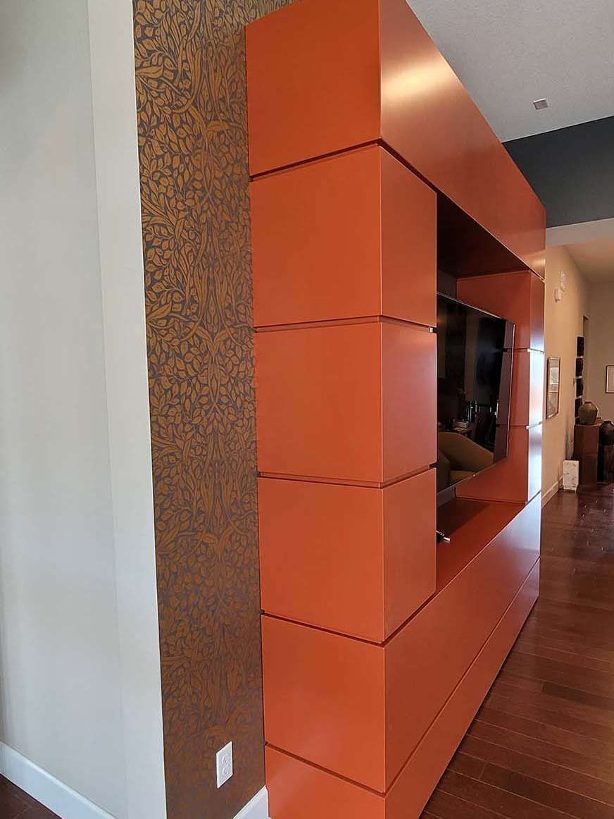 Orange wall unit with a recessed TV, installed against a textured brown wall, in a hallway setting.