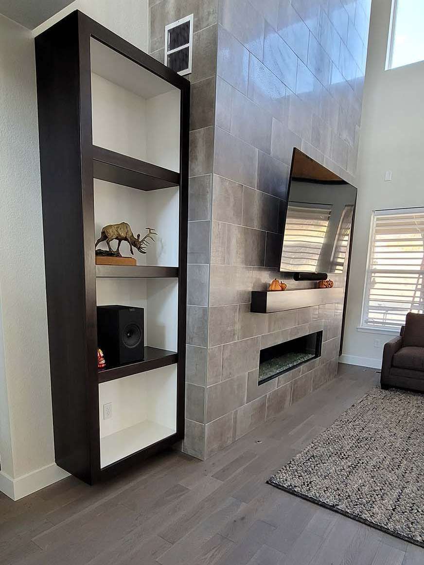 Tall dark brown bookcase with white shelves next to a tiled fireplace with a mounted TV.