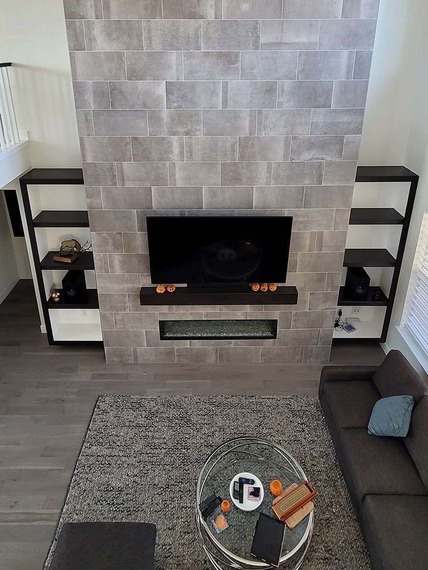 Living room with stone fireplace, TV, and built-in bookshelves. Gray rug and brown couch.