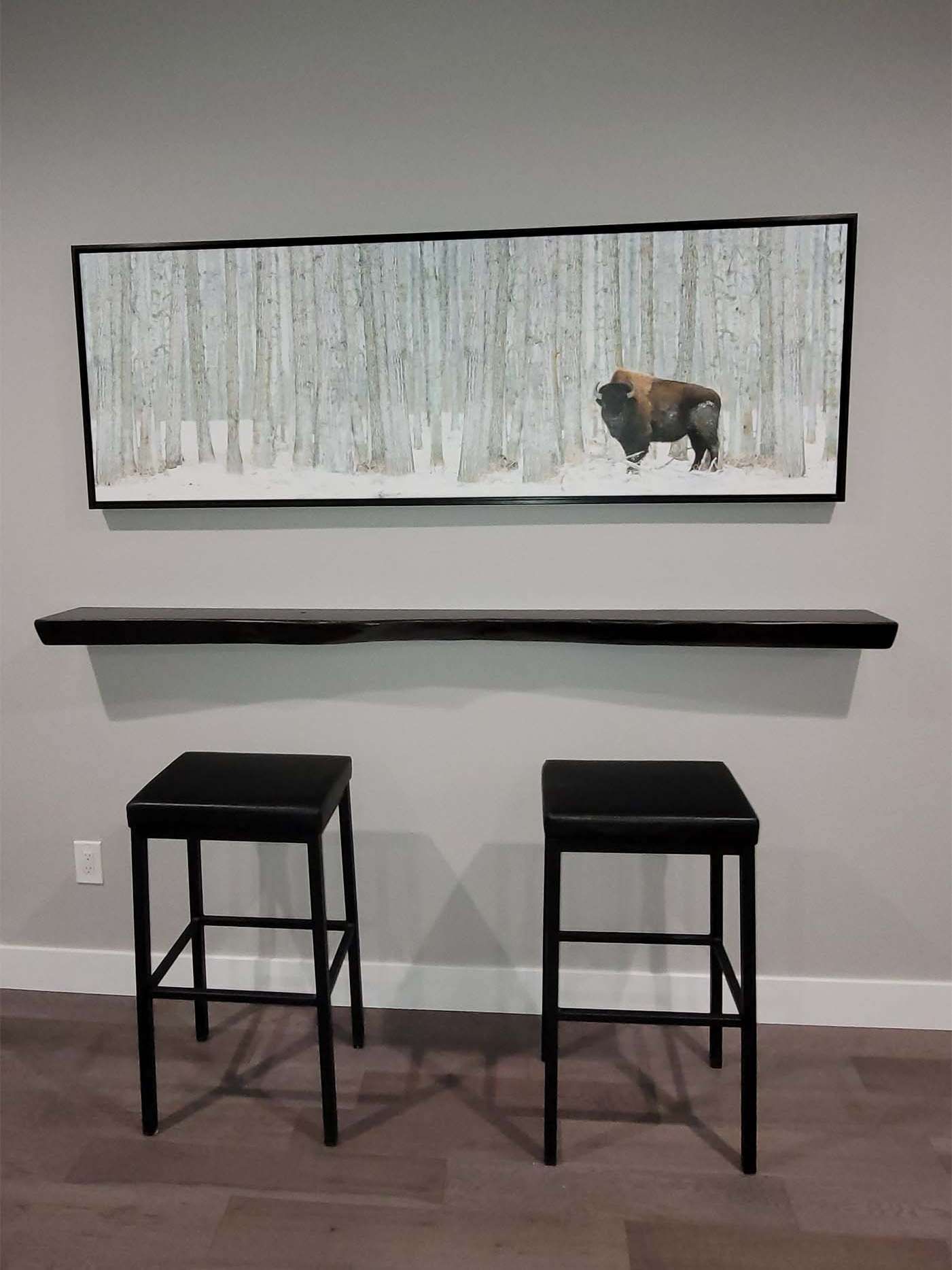 Black bar stools beneath a black shelf and framed artwork of a bison in a snowy forest.