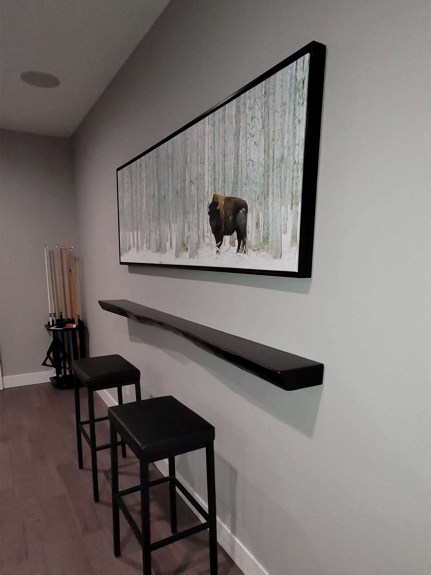 Bar with black stools under a long shelf and a framed image of a bison in a snowy forest.