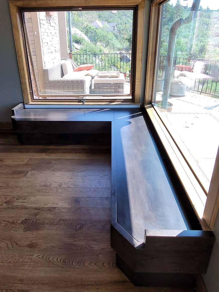 Wooden window seat with dark trim against a large window overlooking an outdoor patio.