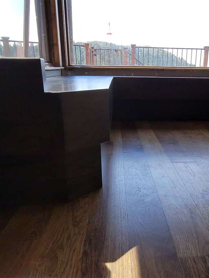Wooden steps inside a room with a view of an outdoor balcony and a mountain range. Sunlight shines on the wooden floor.