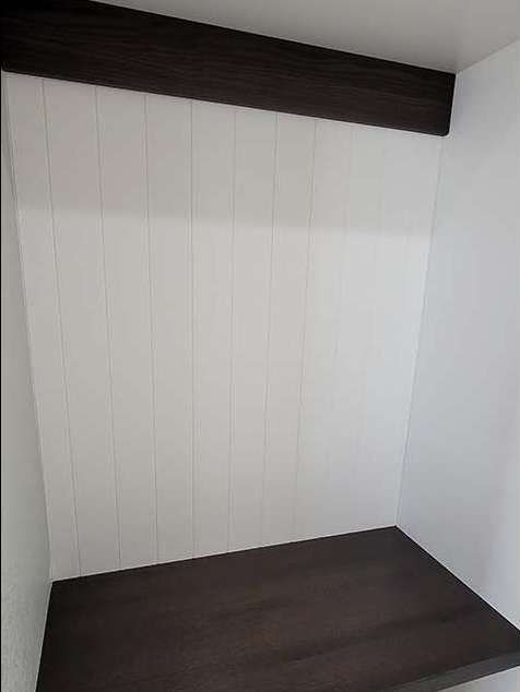 A small alcove with dark wood trim and a dark wood shelf, white vertical paneling.
