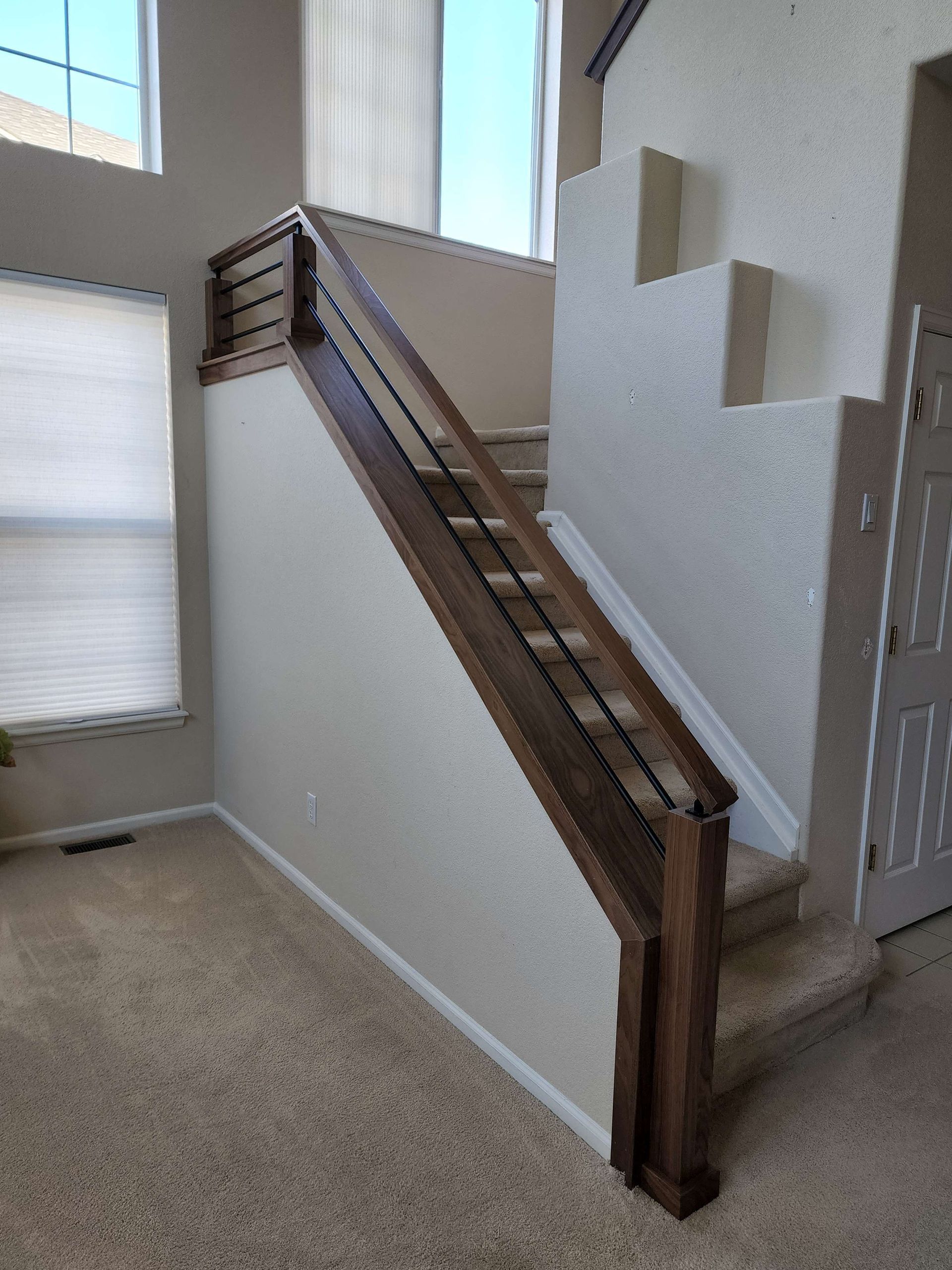 Staircase with brown wooden railing, leading upwards. Cream walls, carpeted stairs, and a window are visible.