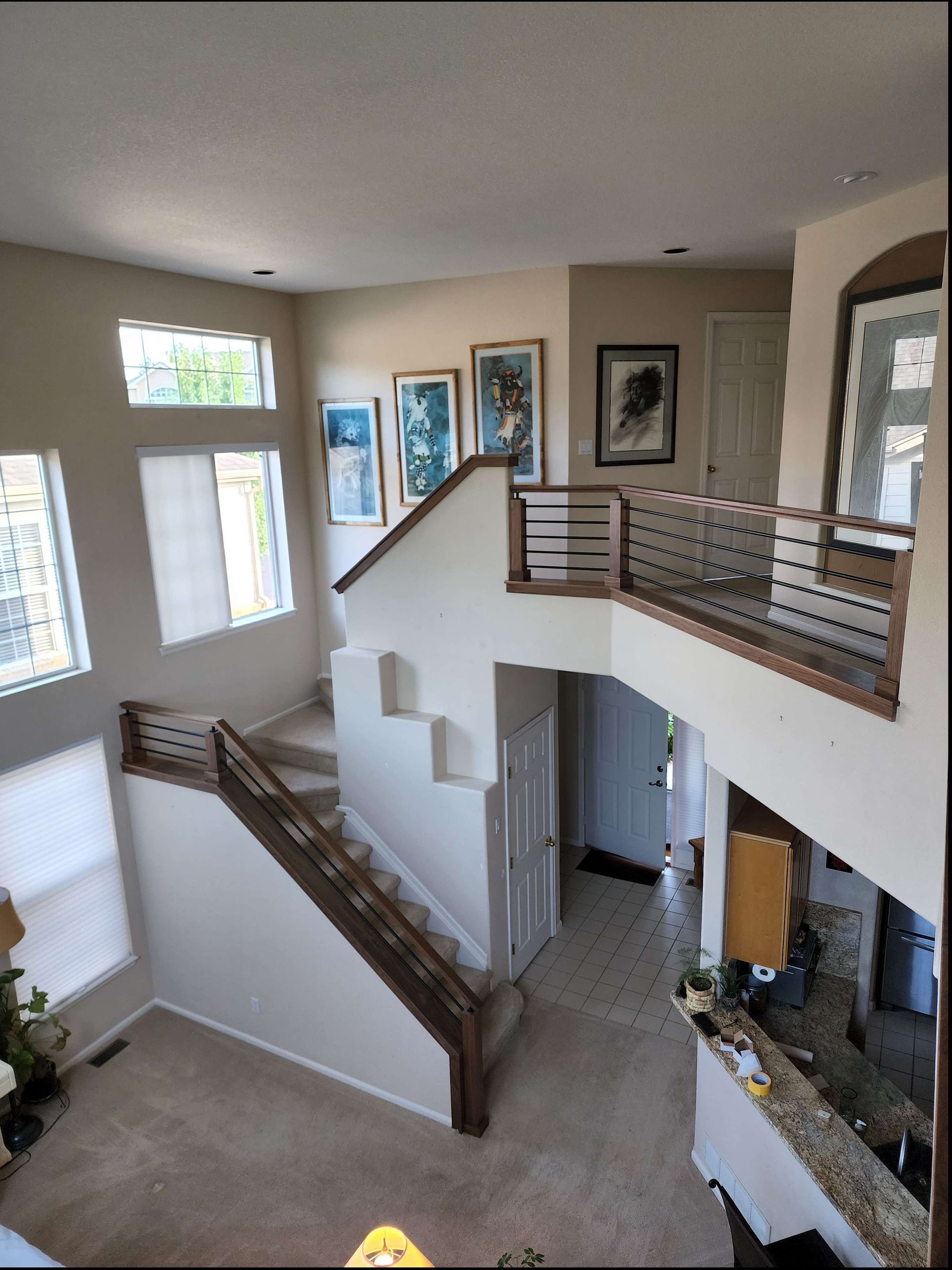 Interior view of a two-story home with a staircase, artwork, and a balcony. Beige walls, wood accents, and windows.